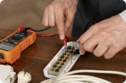 Technician using orange digital multimeter to test wiring inside a white terminal block