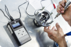 Technician inspecting a vehicle wheel hub bearing assembly with a digital gauge and screwdriver